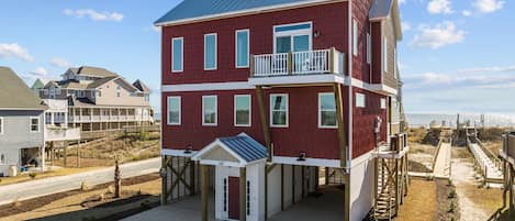 A multi-story house with a balcony on the second floor, a covered entryway, and a view of the beach.