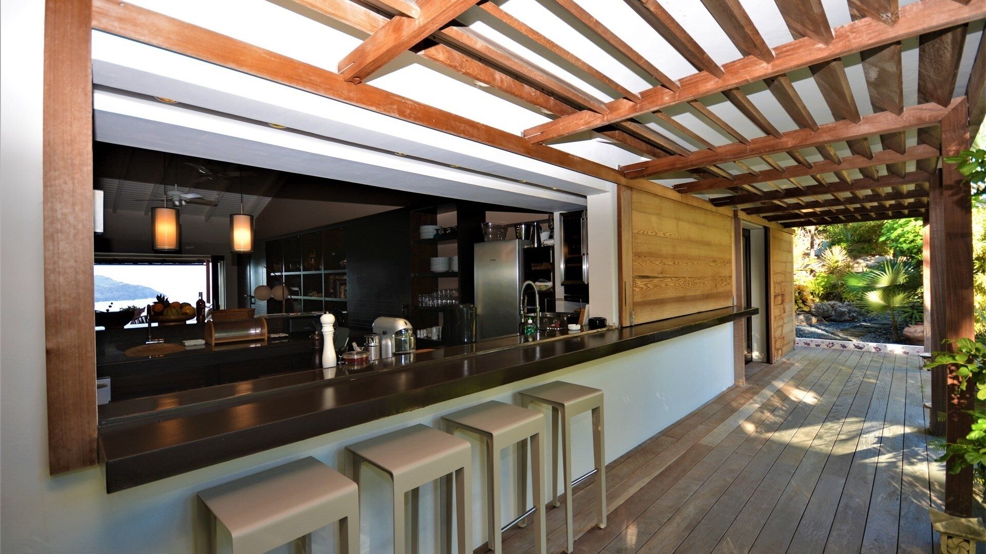 A modern kitchen with a wooden pergola, a bar area with stools, and a view of a mountainous landscape.