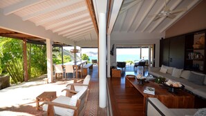 A spacious living area with a view of the sea, wooden furniture, and a large window. - Amancaya Luxury villa (Anse Des Cayes)