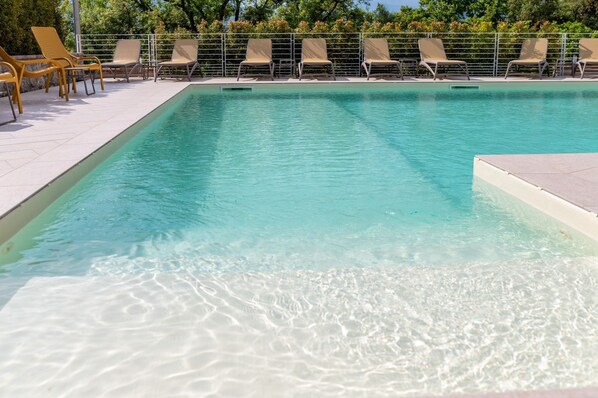 A clear swimming pool with lounge chairs and a tiled deck.