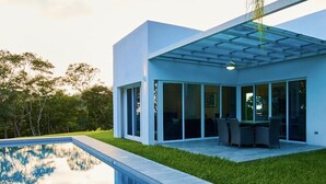 Une maison moderne dotée d’une piscine, de grandes fenêtres et d’un patio couvert.