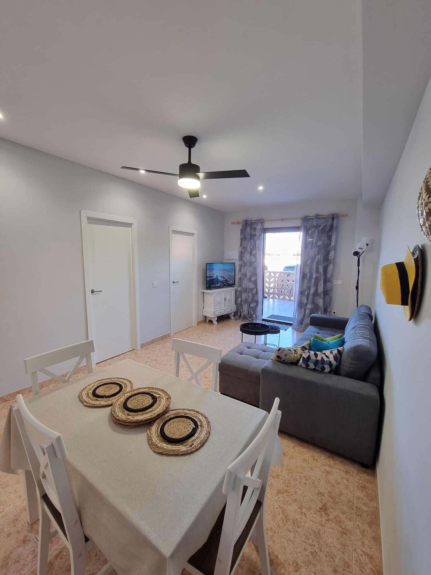 Ein modernes Wohnzimmer mit Essbereich, Deckenventilator, Fernseher und einer Couch mit Kissen.