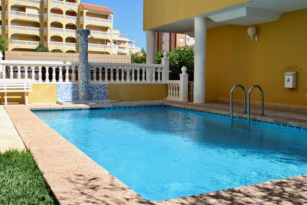 A swimming pool with a tiled edge, a white balustrade, and a building with balconies in the background.