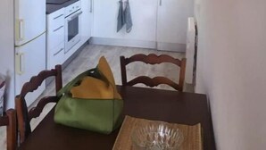 Pieni keittiö, jossa on valkoiset kaapit, liesi ja pesuallas. Keittiössä on pöytä ja tuolit sekä vihreä laukku pöydällä.