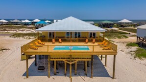 Una casa de playa con piscina, sillas de deck y vista al océano.