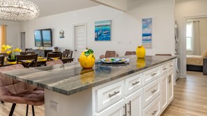 Una cocina moderna con una isla de mármol, armarios blancos y un comedor con sillas y una mesa de madera.