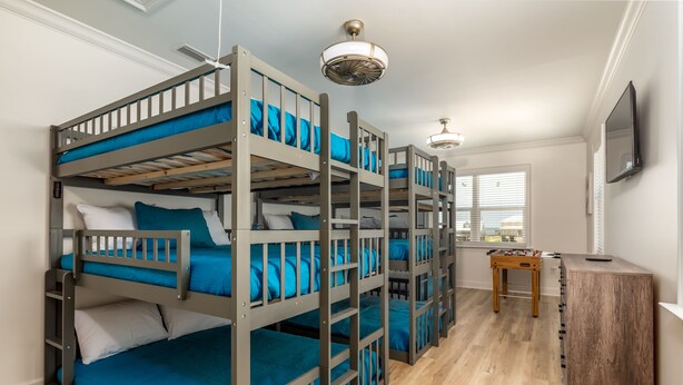 A room with bunk beds, a wooden table, and a TV mounted on the wall. - Oceanfront, pool, oversized deck, volleyball pit! - Lemon Breeze (Dauphin Island)
