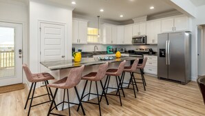 Cocina moderna con armarios blancos, un refrigerador de acero inoxidable y una barra con cuatro taburetes.