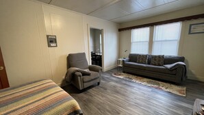 Et værelse med sofa, lænestol og et lille bord med lampe.