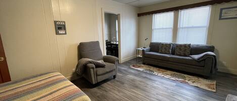 A room with a sofa, armchair, and a small table with a lamp.