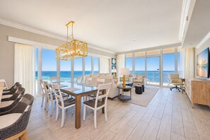 A spacious room with a large dining table, multiple chairs, a television, and a view of the ocean.
