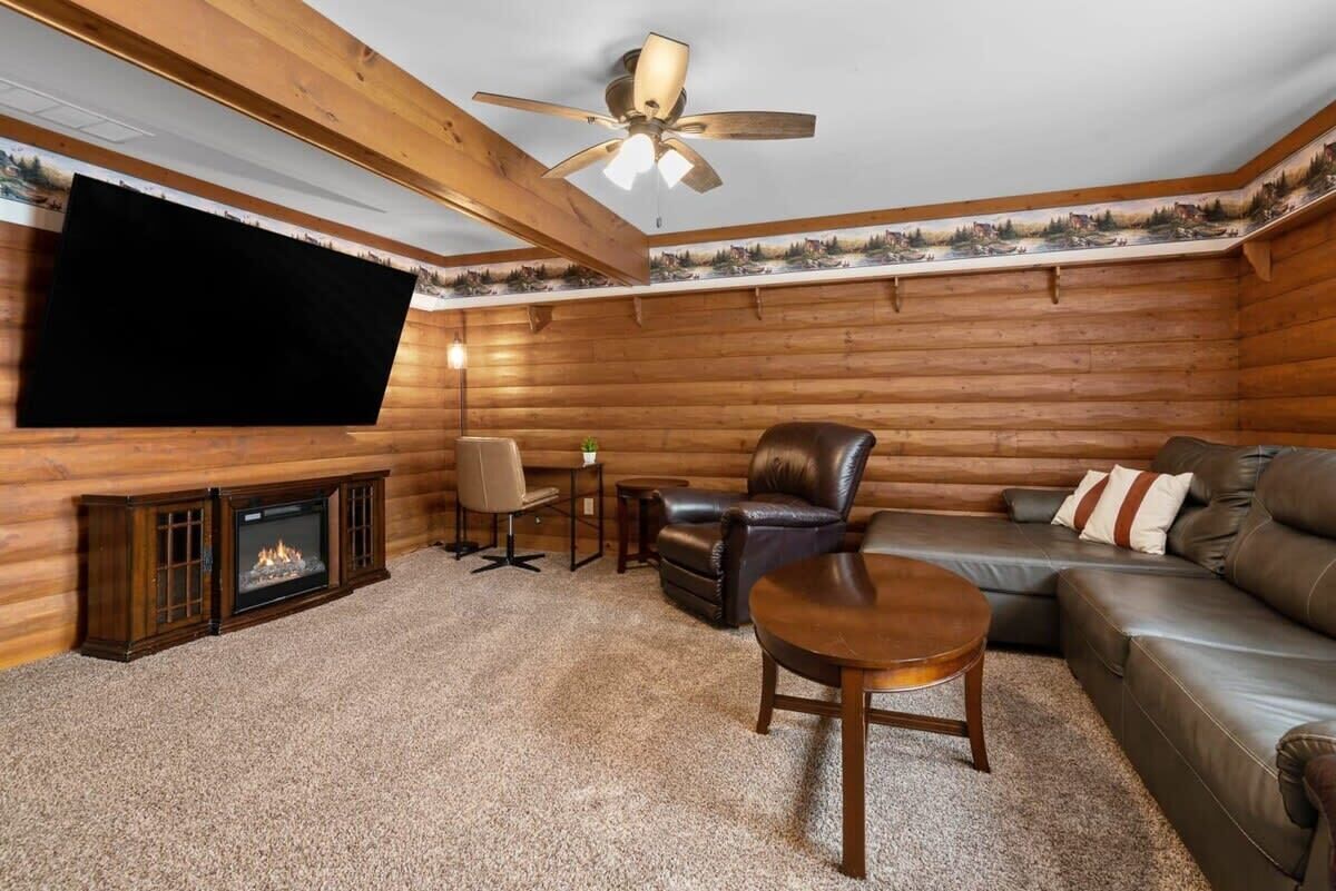 A log cabin interior with a fireplace, leather seating, a television, and a ceiling fan.