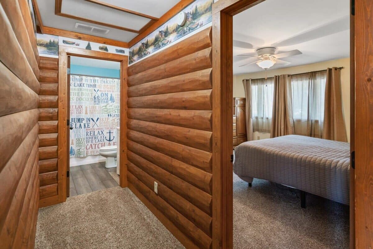 Une pièce aménagée dans le style d’un chalet en rondins, avec un lit, un ventilateur de plafond et une salle de bain équipée de toilettes et d’une douche.