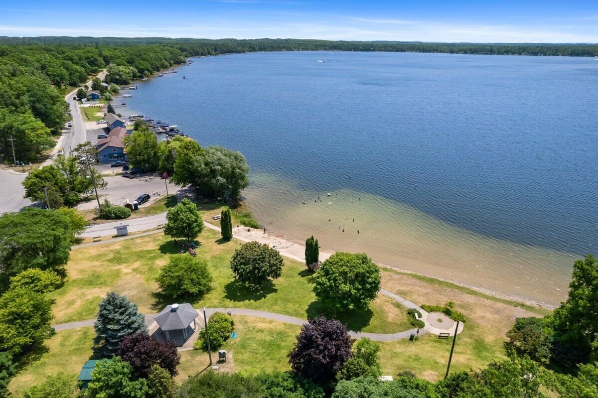 Ein Luftbild eines Sees mit einer Liegenschaft, einem Parkplatz, einem Strand und einer Reihe von Häusern am Ufer.