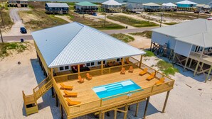 Una casa frente al mar con piscina, terraza de madera y mobiliario exterior.