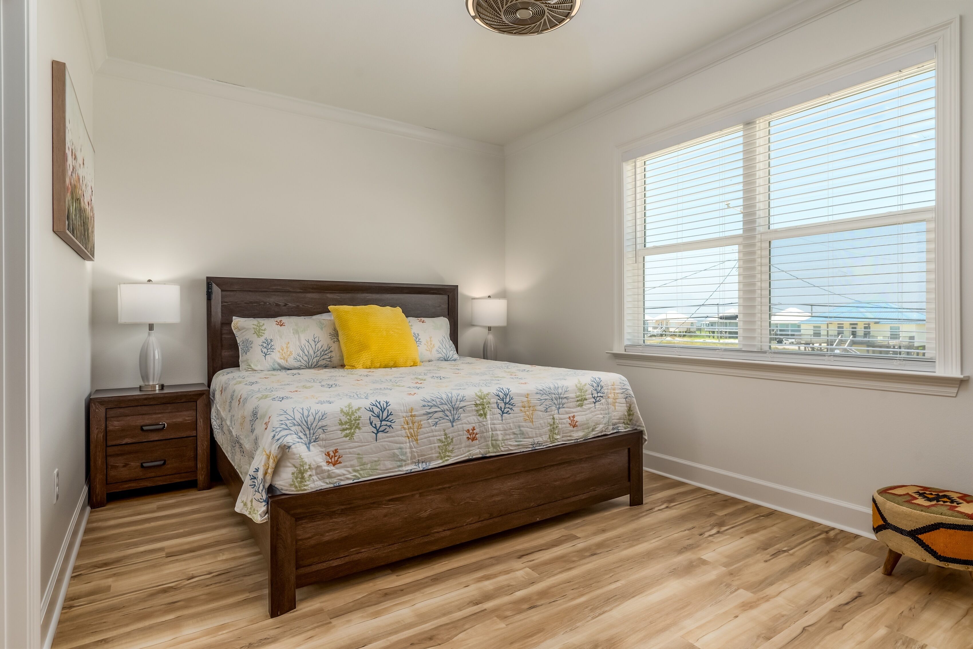 A bedroom with a wooden bed, a nightstand, a lamp, and a window with blinds.