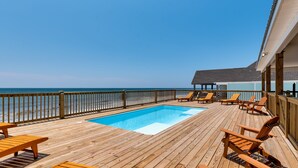 Una terraza de madera con piscina, sillas de descanso y vista al océano.