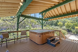 A wooden deck with a hot tub, chairs, and a wooden railing overlooking a forested area. - Heavenly Hilltop - 3-Level Home with Game Room by Yosemite Region Resorts (Groveland)