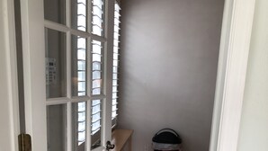 A narrow hallway with a white door on the left, a window with blinds, a wooden bench, and a trash can. - Bay View Bungalow By The Pier 4 Bedroom Home by RedAwning (Norfolk)
