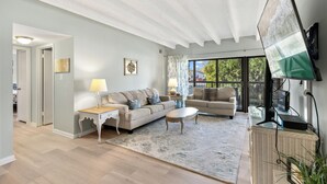 Un salon spacieux avec un plafond haut, une grande fenêtre, un téléviseur à écran plat et un coin salon confortable.