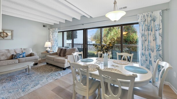 Un salon spacieux avec une grande table à manger, des meubles blancs et une vue sur l’extérieur grâce à de grandes fenêtres.