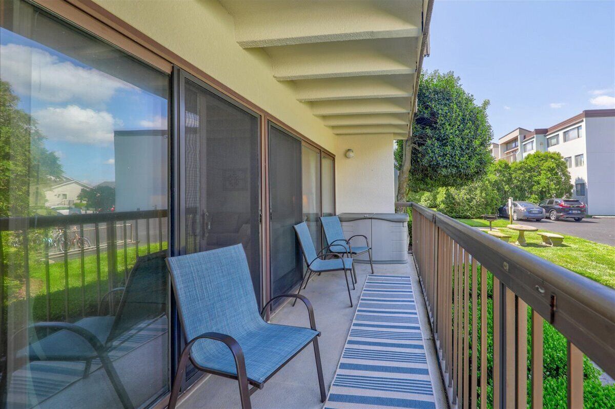 A balcony with two chairs and a table, overlooking a street with parked cars and greenery.