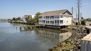 A waterfront house with a dock, a stone breakwater, and a clear view of the water. - Bliss on the Bay by Seaside Vacations & Sales (Chincoteague Island)