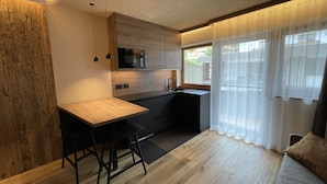 Eine moderne Küche mit Holzarbeitsplatte, schwarzen Barhocker, einer eingebauten Mikrowelle und einem Fenster mit durchsichtigen Vorhängen.