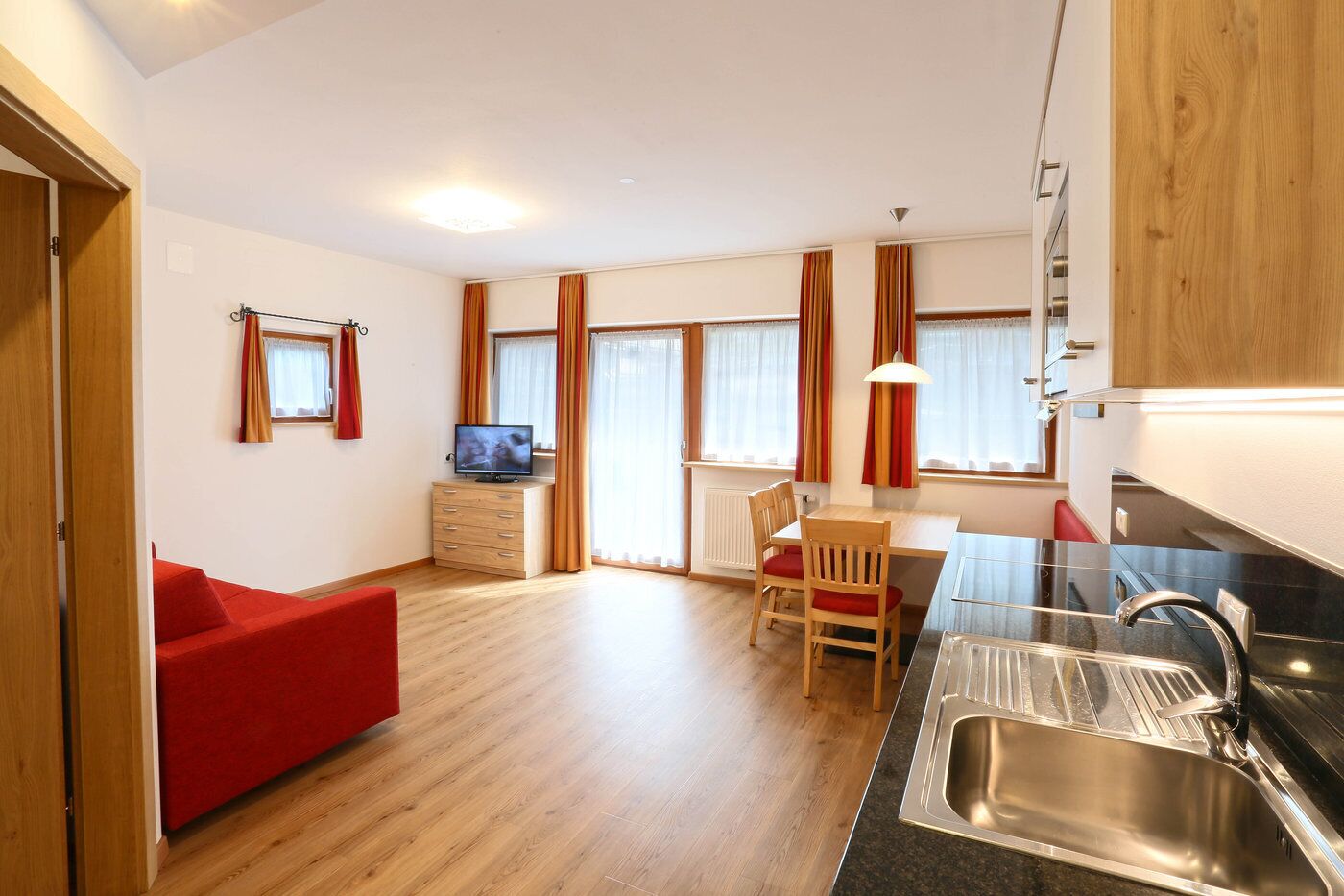Ein kompakter Wohnbereich mit Küchenzeile, Essbereich und einem roten Sofa.