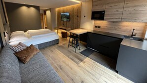 Ein modernes Hotelzimmer mit Bett, einer Couch, einer kleinen Küchenzeile und einem an der Wand befestigten Fernseher.