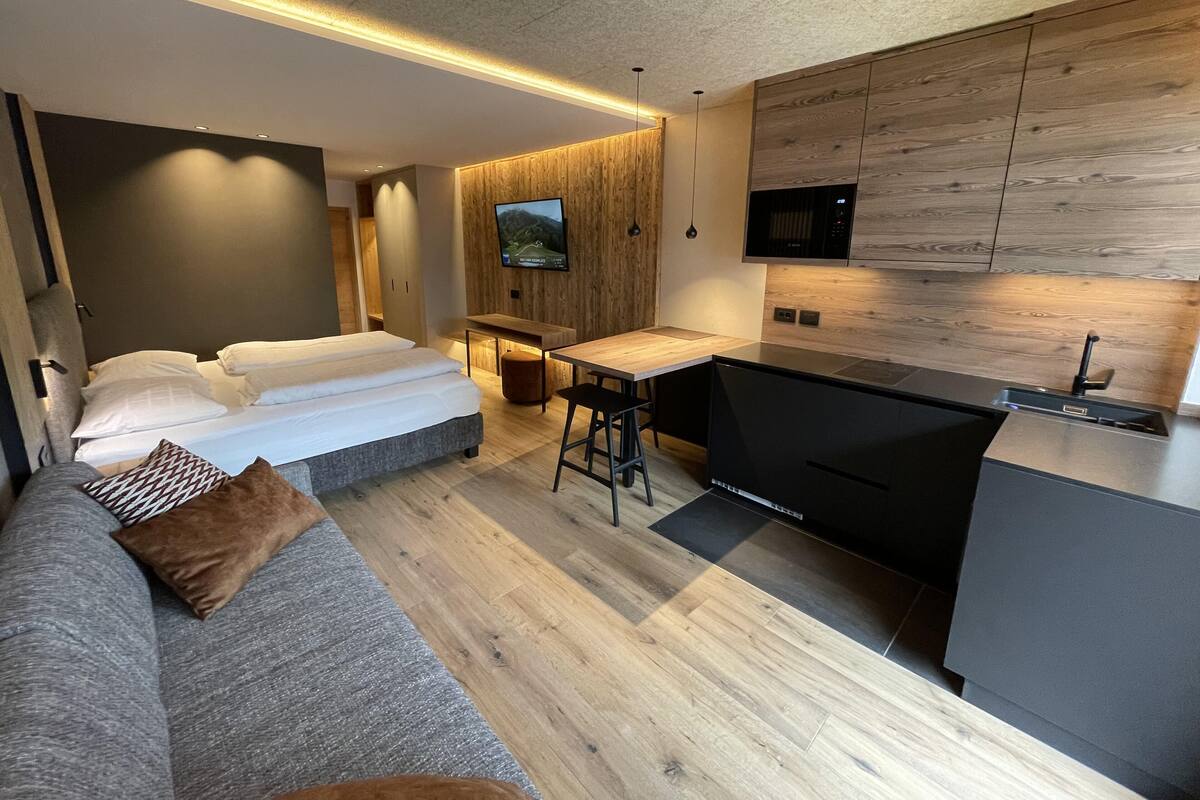 Ein modernes Hotelzimmer mit Bett, einer Couch, einer kleinen Küchenzeile und einem an der Wand befestigten Fernseher.