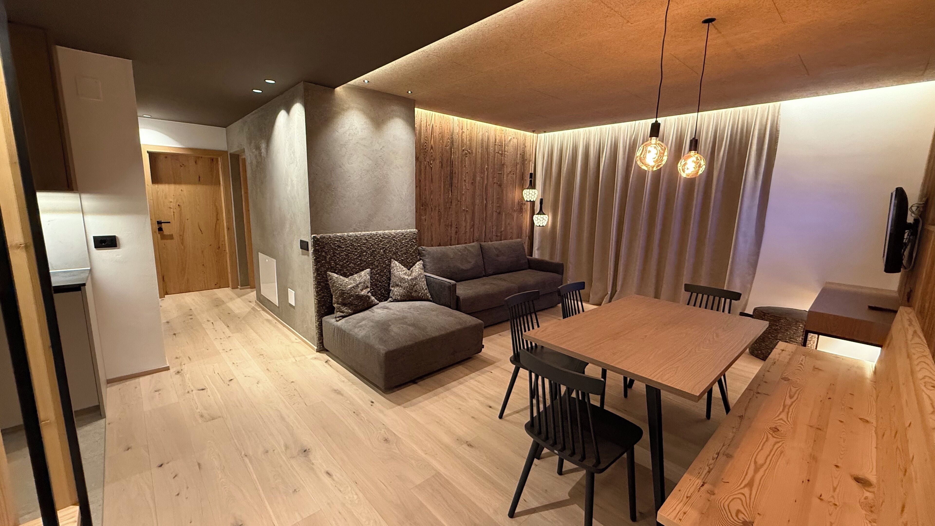 A modern living space with a wooden dining table, a sofa, and a kitchen area.