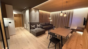A modern living space with a wooden dining table, a sofa, and a kitchen area. - Residence Tantalus (San Lorenzo di Sebato)