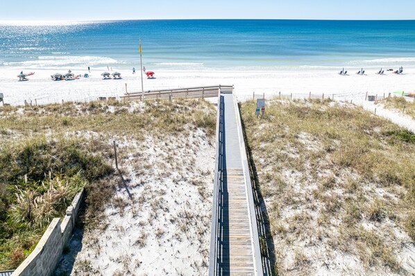 A beach with a wooden boardwalk leading to the shore, sandy dunes, and a clear view of the ocean.