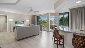 A spacious living area with a sofa, TV, and a balcony with a view of the outdoors. - Beach Front - Heated Pool- Partial View- 2BR Gullwing #203 (Fort Myers Beach)