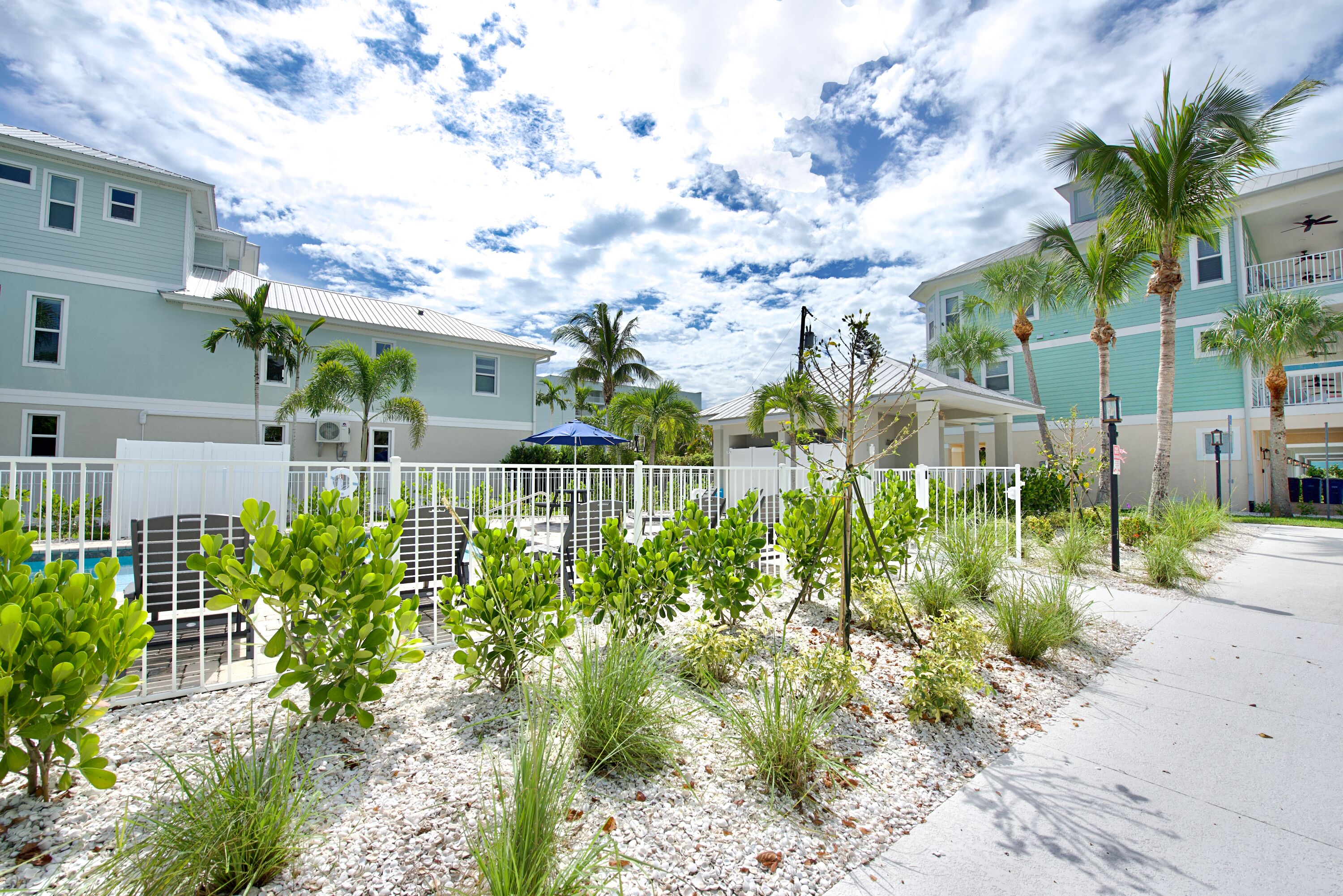 A residential area with houses, palm trees, and a white fence.