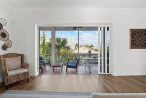 A spacious balcony with a wooden floor, a wicker chair, and two blue chairs.