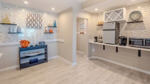 Una cocina moderna con refrigerador empotrado, microondas y cafetera. Hay estantes decorativos con diversos objetos y un salpicadero con patrón de espiga.