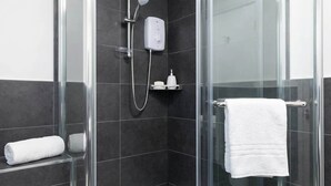 A glass-enclosed shower with a handheld showerhead, a soap dispenser, and a towel rack with a white towel.