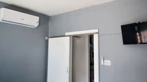 Ein Zimmer mit grauer Wand, einer weißen Klimaanlage, einer Tür und einem angebrachten Fernseher.