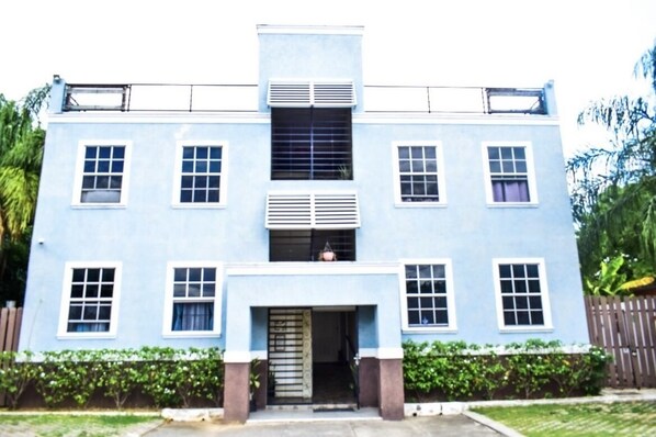 A two-story building with a symmetrical facade, large windows, and a central entrance with a door and steps. - Up Town Kingston- Romantic Sky view- 5 mins Boulevard Super Centre (Kingston)