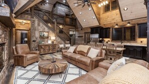 Ein geräumiger Wohnbereich mit hoher Decke, Holzbalken, Kamin, großzügigem Sofa, Couchtisch und einer Treppe, die in einen oberen Bereich führt.