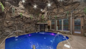 Ein Whirlpool mit grottenförmigem Innenraum aus Felsen, einer Holzterrasse und einer Glastür zum Außenbereich.