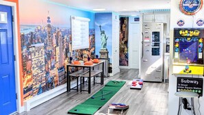 A room with a cityscape mural, a table with orange plates, a green mat, and a Pac-Man game.