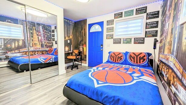 A room with a bed featuring a basketball theme, a large mirror, a blue door, and subway station signs on the walls.