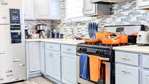 A modern kitchen with light blue cabinets, a black stove with orange pots, and a tiled backsplash.