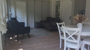 Een ruime kamer met een hoge plafond en een plafondventilator. Er is een zithoek met een tafel en stoelen, en een bank achterin.