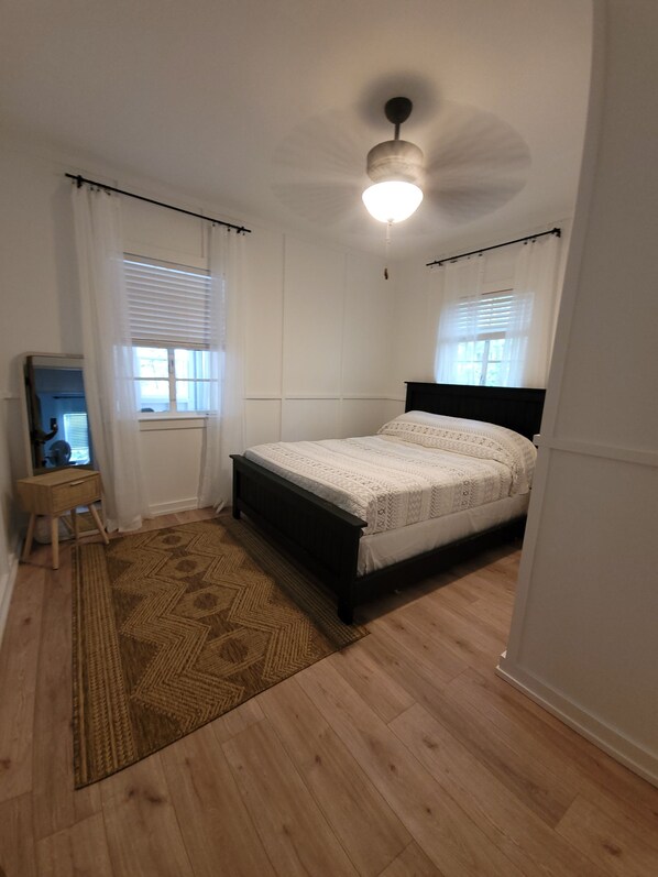 A bedroom with a bed, a standing lamp, a mirror, and a window with blinds.