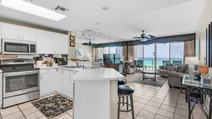 Cozinha moderna com ilha central, sala de jantar com vista para o oceano e sala de estar com sofá e mesa.