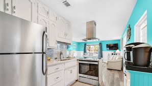 Une cuisine moderne avec des meubles blancs, des appareils en acier inoxydable et un mur d’accent de couleur turquoise.